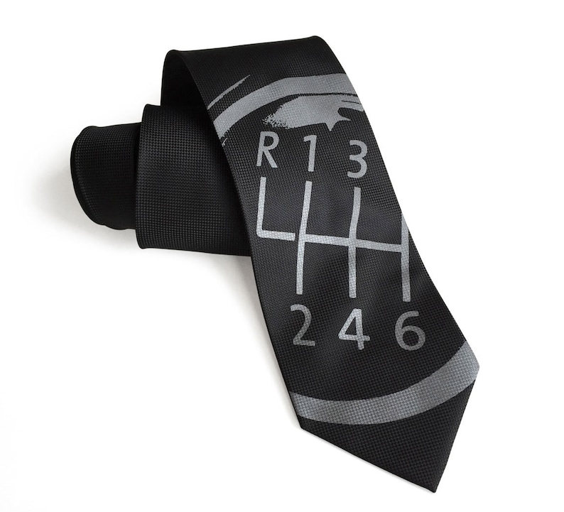May include: A black silk tie with a silver gray gear shift pattern and the numbers R, 1, 3, 4, 5, 6, and 2.