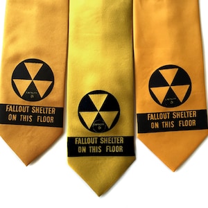 May include: Three yellow neckties featuring a black radiation symbol and a black horizontal band with the text "FALLOUT SHELTER ON THIS FLOOR" printed in yellow. Each tie displays a circular emblem with the radiation icon and the word "CAPACITY" printed inside the bottom triangle of the symbol.