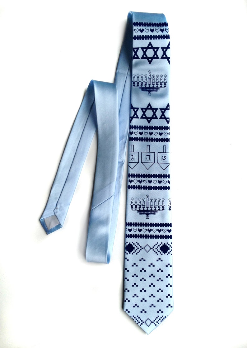 May include: Light blue tie with a repeating pattern of Star of David, menorah, dreidel, and heart symbols in navy blue. The tie is made of a smooth, satin-like material.