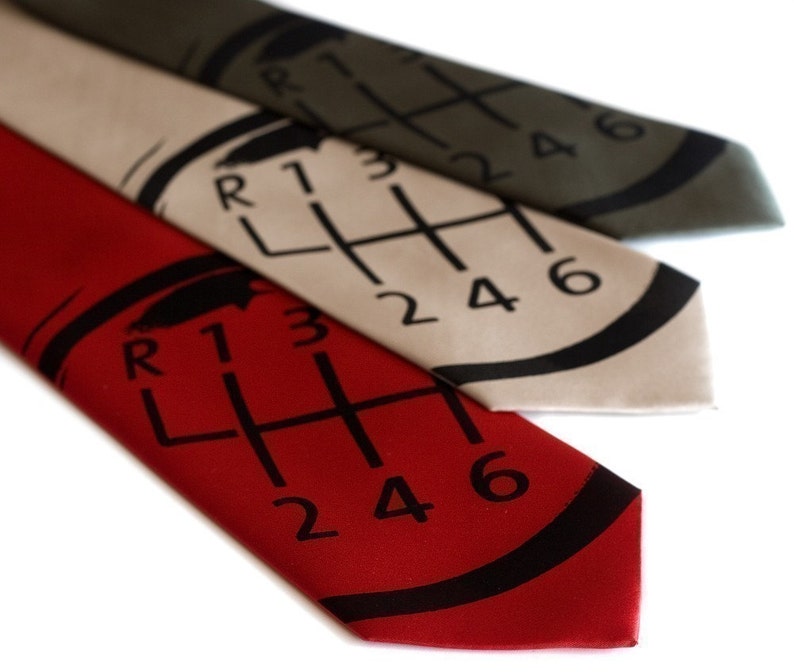 May include: Three silk ties with a gear shift pattern printed on them. The ties are red, beige, and olive green.