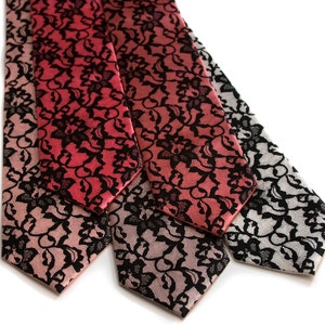 May include: Three silk neckties with a black lace pattern on a gradient background. The ties are in shades of pink, red, and gray.