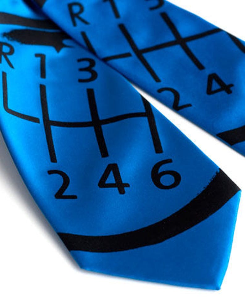 May include: A blue tie with a black gear shift pattern and the numbers 1, 2, 3, 4, 5, and 6 printed on it.