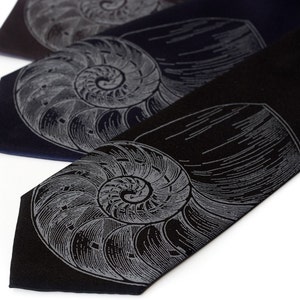May include: Three black neckties with a nautilus shell design printed in silver. The ties are arranged in a stack, with the top tie being the darkest shade of black.