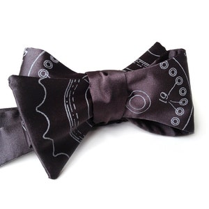 May include: A dark brown bow tie with a white patterned design. The pattern is a circuit board with the number 19 printed on it.