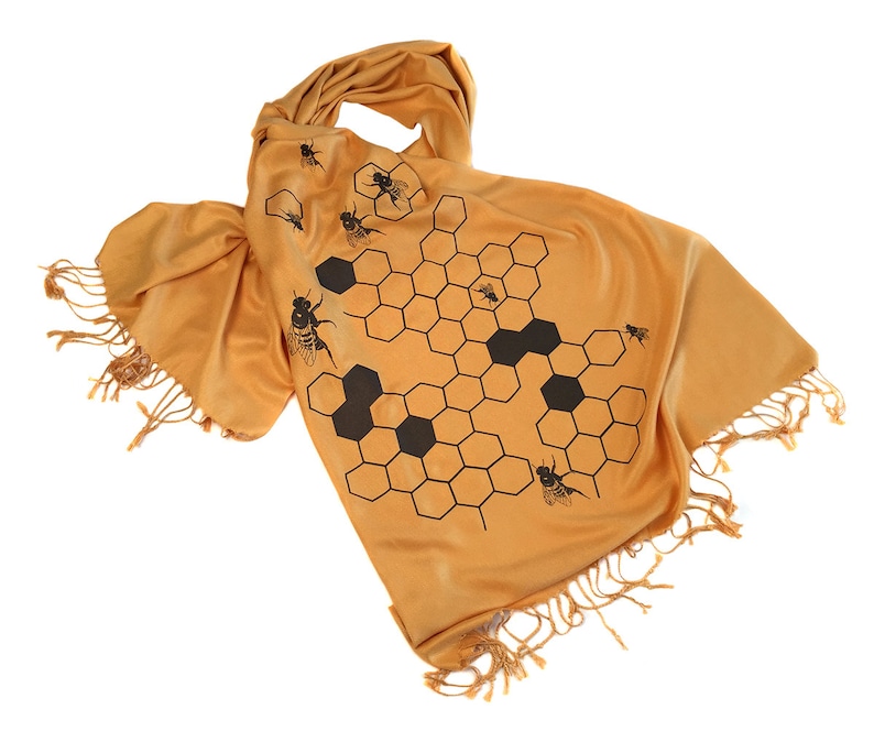 May include: A mustard yellow scarf with a black honeycomb pattern and bees. The scarf has fringe on the ends.