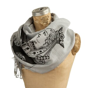 May include: A gray scarf with a black and white print of the Queen of Spades playing card. The scarf is draped over a mannequin's neck.