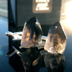 May include: A pair of silver cufflinks with clear, faceted crystal accents. The crystals are shaped like points and have a smoky gray color.
