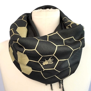 May include: Black infinity scarf with a gold honeycomb pattern and a gold bee design.