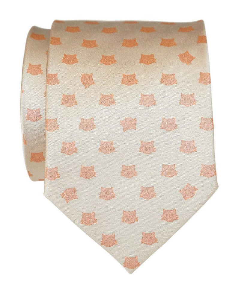 Puede incluir: Una corbata de seda color crema con un patr&oacute;n repetido de caras de gatos naranjas.
