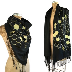 May include: Black scarf with a gold honeycomb and bee design. The scarf has fringe on the edges.