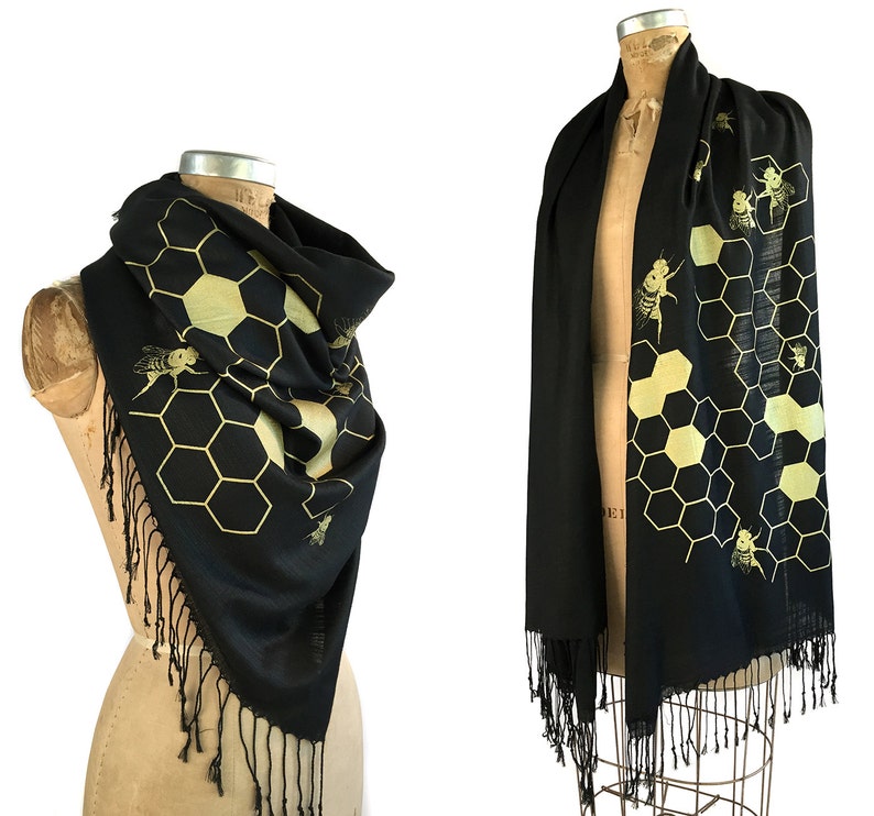 May include: Black scarf with a gold honeycomb and bee design. The scarf has fringe on the edges.
