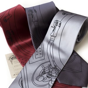 May include: Three silk ties featuring a black and white design of a record player. The ties are in grey, red, and dark grey.