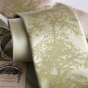 May include: A light green silk tie with a gold tree design. The tie is hand-screened and made with fair trade silk. The tag reads "Specializing in: Hand-Silkscreened Neckties Fair Trade Woven Silk Scarves Available in 100% Silk"