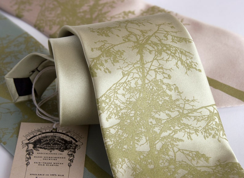 May include: A light green silk tie with a gold tree design. The tie is hand-screened and made with fair trade silk. The tag reads "Specializing in: Hand-Silkscreened Neckties Fair Trade Woven Silk Scarves Available in 100% Silk"