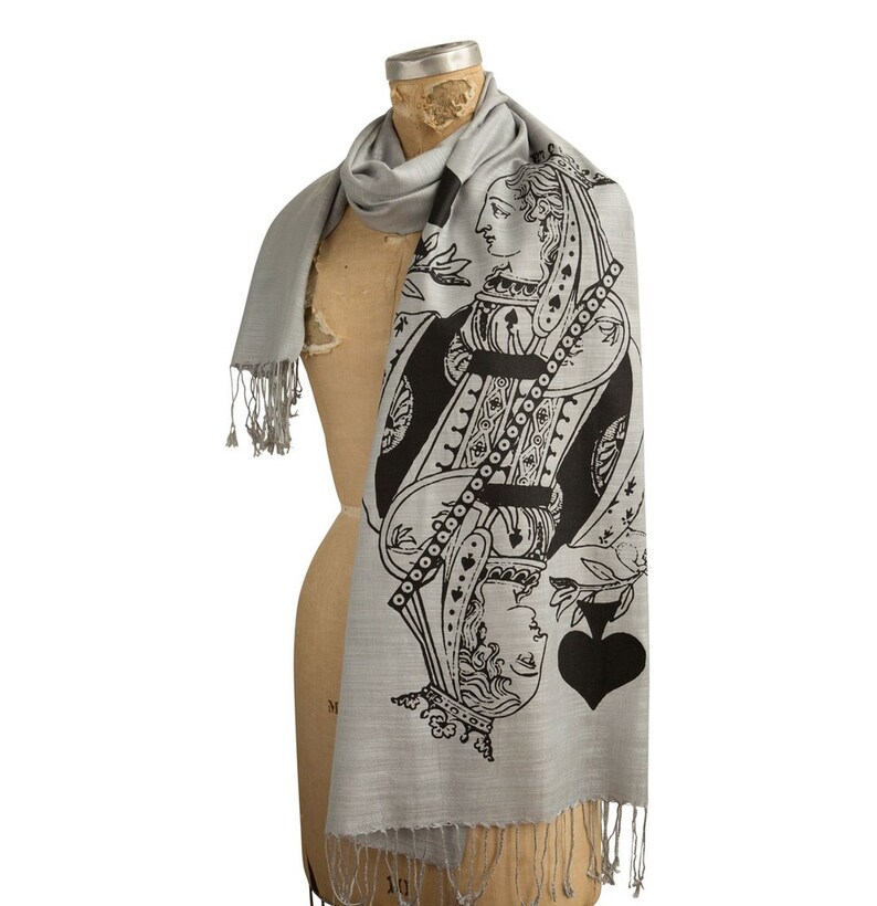 May include: A gray silk scarf with a black and white print of the Queen of Spades playing card. The scarf has a fringe border.