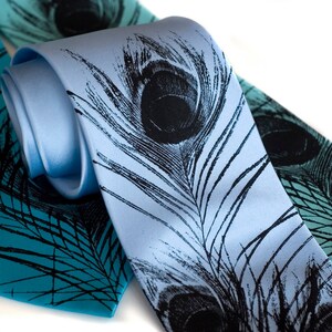 May include: Two silk neckties with a peacock feather design. One tie is light blue with black feathers, and the other is teal with black feathers.