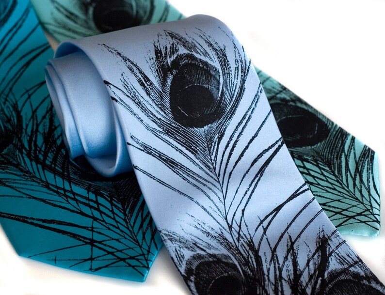 May include: Two silk neckties with a peacock feather design. One tie is light blue with black feathers, and the other is teal with black feathers.