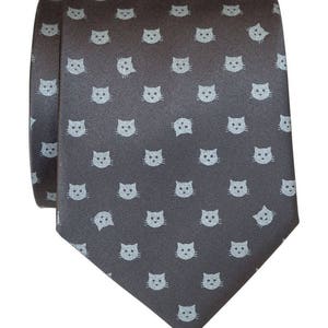 Puede incluir: Una corbata gris oscuro con un patr&oacute;n repetido de caras de gato azul claro.