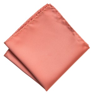 Puede incluir: Un pa&ntilde;uelo de bolsillo de color rosa coral, doblado y listo para colocar en el bolsillo de la chaqueta de un traje.