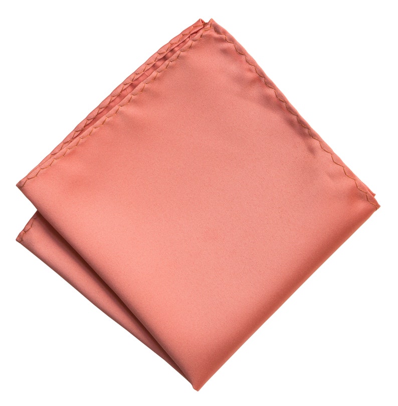 Puede incluir: Un pa&ntilde;uelo de bolsillo de color rosa coral, doblado y listo para colocar en el bolsillo de la chaqueta de un traje.