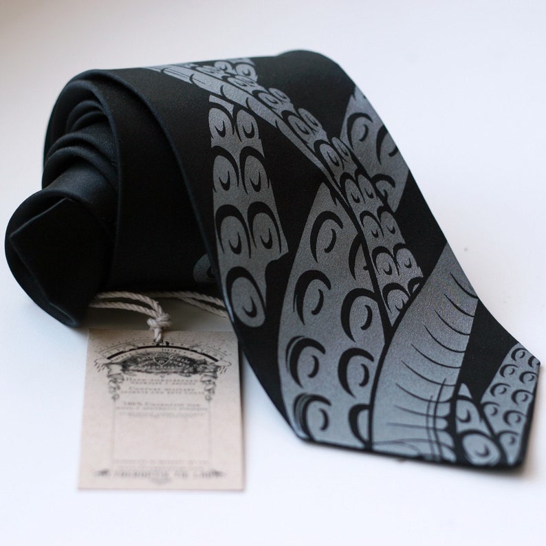 Puede incluir: Una corbata de seda negra con un dise&ntilde;o de pulpo gris plateado. La corbata tiene una etiqueta adjunta con el texto "The Kraken of the Sea".