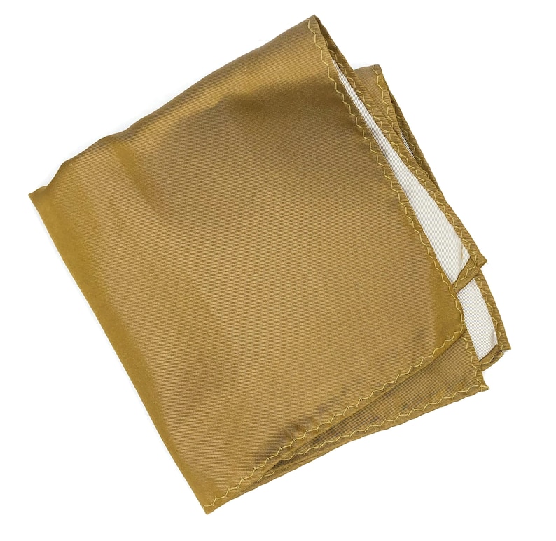 Op de afbeelding: Een gouden zakdoek met een witte gestikte rand. De zakdoek is gevouwen en klaar om in een zak te worden gestoken.