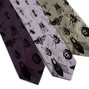 May include: Three silk ties with a black insect pattern on a white background. The ties are in shades of purple, gray, and green.