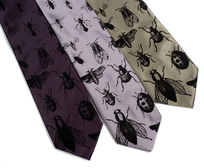 May include: Three silk ties with a black insect pattern on a white background. The ties are in shades of purple, gray, and green.