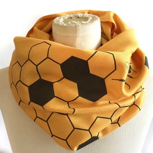 May include: A yellow scarf with a black honeycomb pattern. The scarf is folded and displayed on a white mannequin.
