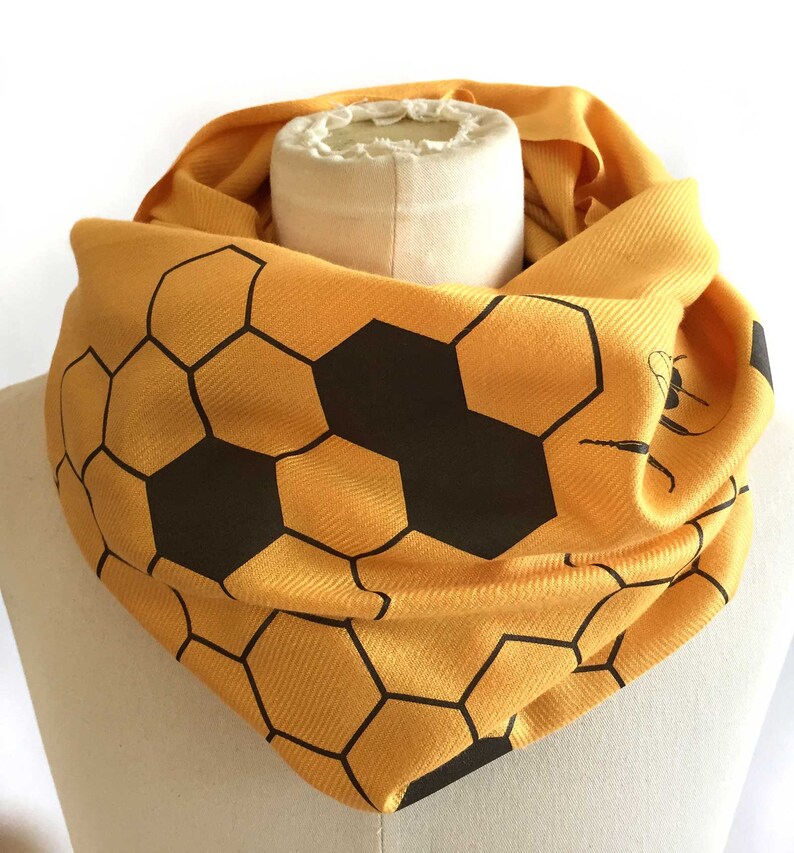 May include: A yellow scarf with a black honeycomb pattern. The scarf is folded and displayed on a white mannequin.