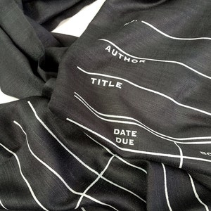 May include: Black fabric scarf with white lines and the words "AUTHOR", "TITLE", "DATE DUE", and "BORROWER" printed on it.