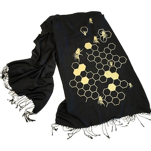 May include: Black scarf with a gold honeycomb pattern and bees. The scarf has fringe on the edges.