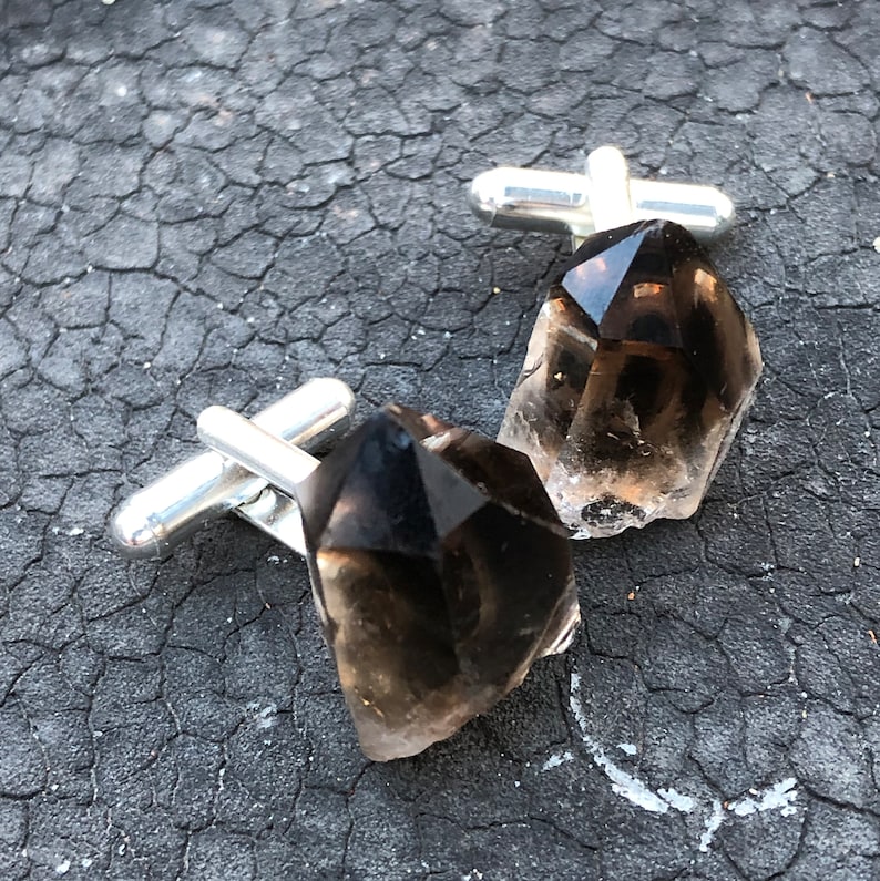 May include: A pair of cufflinks featuring dark brown, faceted, crystal stones set in silver.