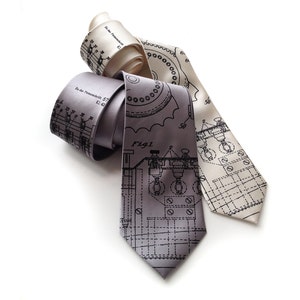 May include: Three silk neckties with a technical blueprint design. One tie is light gray, another is off-white, and the third is a darker gray. The ties are arranged on a white background.