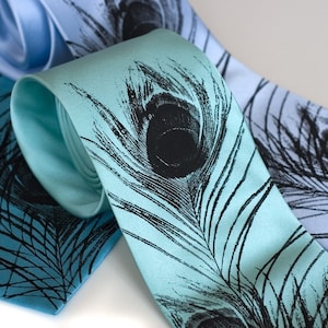 May include: Two silk neckties with a peacock feather design. One tie is light blue and the other is a teal blue.