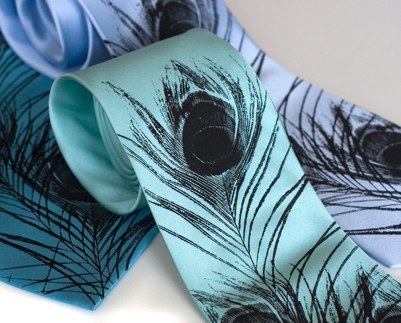 May include: Two silk neckties with a peacock feather design. One tie is light blue and the other is a teal blue.