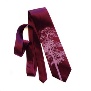 May include: A burgundy silk tie with a light pink silhouette of a tree printed on it.