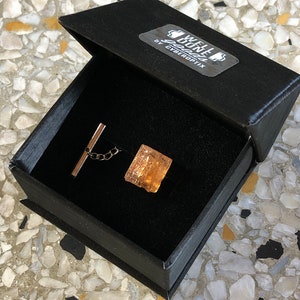 May include: A gold tie tack in a black box with a label that reads "Well Done" by Cyberoptix.
