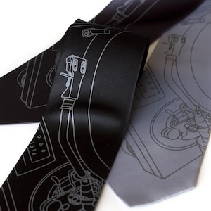 May include: Two black silk ties with a white outline of a record player on them. One tie is gray and the other is black.