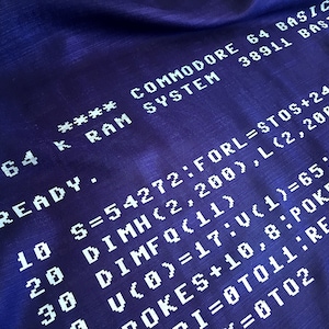 May include: A close-up of a blue fabric with white text that reads "64 K RAM SYSTEM **** COMMODORE 64 BASIC 38911 BASIC READY. 10 S=54272:FORL=STOS+24:POKEL 20 DIMH(2,200),L(2,200),C(2 30 DIMFQ(11) 7OKES+10,8:POKES+22 U(0)=17:V(1)=65:V(2)= I=0T011:READFQ =0T02".