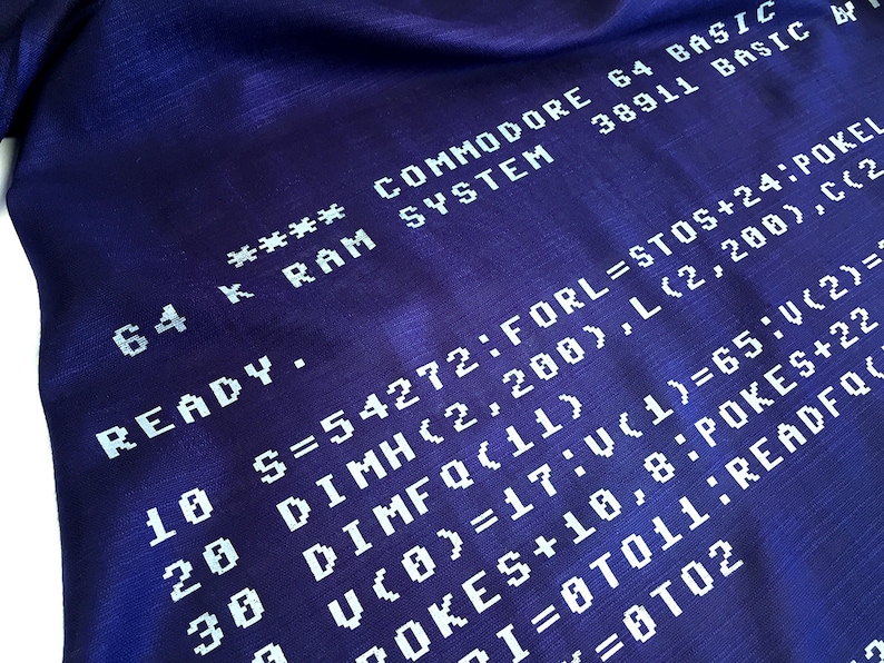 May include: A close-up of a blue fabric with white text that reads "64 K RAM SYSTEM **** COMMODORE 64 BASIC 38911 BASIC READY. 10 S=54272:FORL=STOS+24:POKEL 20 DIMH(2,200),L(2,200),C(2 30 DIMFQ(11) 7OKES+10,8:POKES+22 U(0)=17:V(1)=65:V(2)= I=0T011:READFQ =0T02".