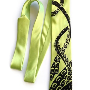 Puede incluir: Una corbata de seda verde lima con un dise&ntilde;o de pulpo negro. El pulpo se representa con tent&aacute;culos que se envuelven alrededor de la corbata.