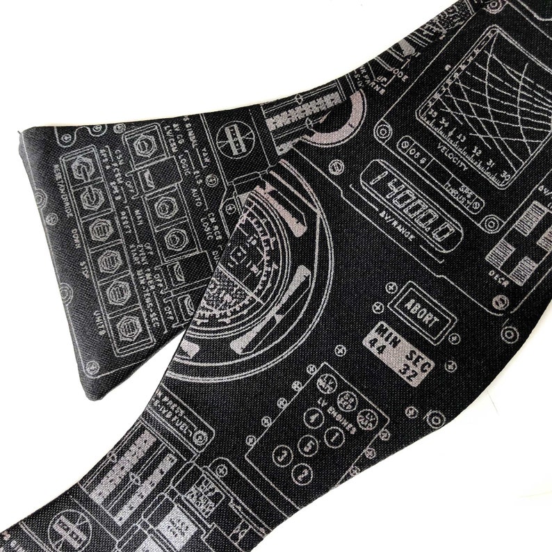 Puede incluir: Pajarita negra con un dise&ntilde;o blanco de un panel de control de nave espacial con botones, diales y medidores. El texto en el panel incluye "Abort", "Min Sec", "LV Engines" y "Velocity".