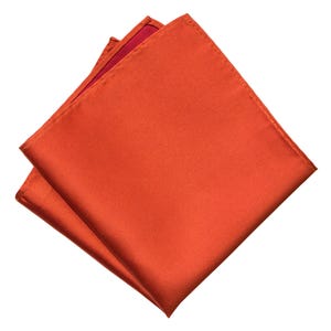 Op de afbeelding: Een gevouwen oranje zijden zakdoek. De vierkant is dubbelgevouwen en de randen zijn zichtbaar.