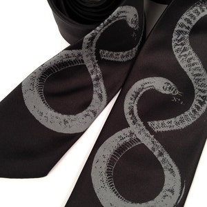 May include: A black silk tie with a gray snake design. The snake is depicted in a coiled position, with its head raised and its tongue flicking out.