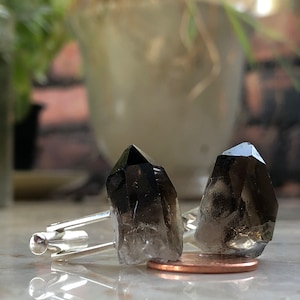 May include: A pair of cufflinks featuring two dark smoky quartz crystals set in silver.