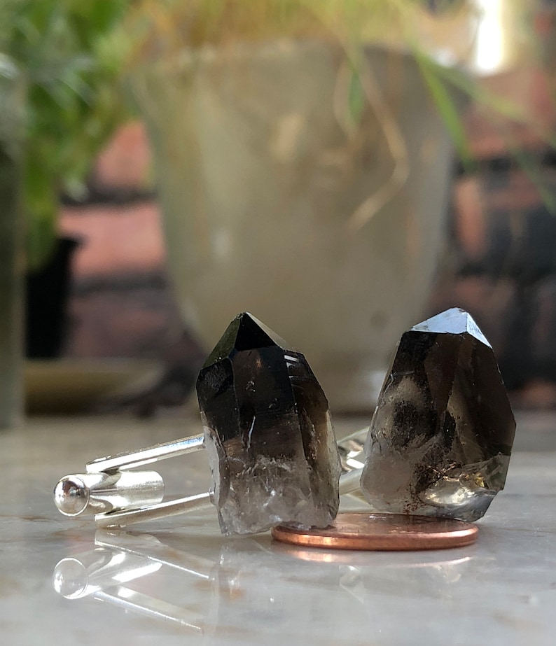 May include: A pair of cufflinks featuring two dark smoky quartz crystals set in silver.