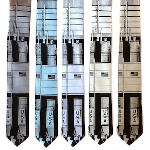 Pode incluir: Cinco gravatas de seda com uma estampa gráfica em preto e branco de um edifício com o texto "United States" e "USA" nas gravatas. As gravatas são em diferentes tons de azul e cinza.