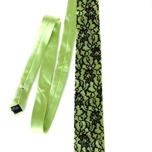 May include: A green silk tie with a black lace pattern. The tie is tied and the loose end is hanging down.