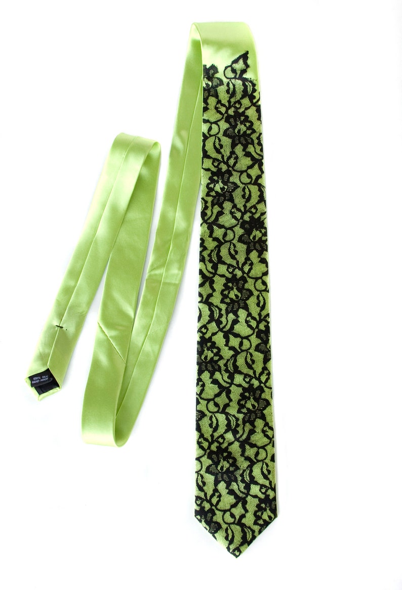 May include: A green silk tie with a black lace pattern. The tie is tied and the loose end is hanging down.